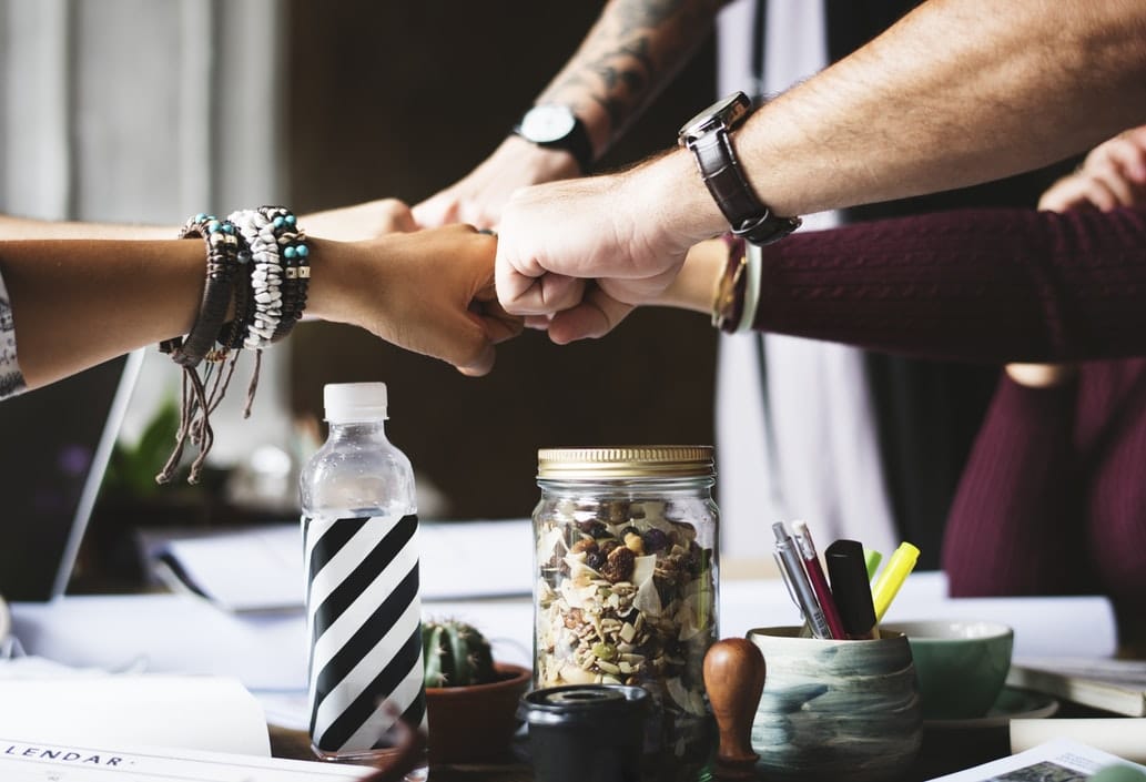 Five people doing a group fist bump over a table