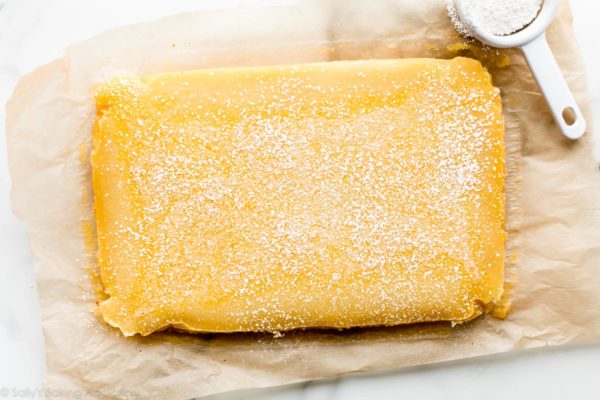 a bright yellow citrusy lemmon bar with sugar on top.