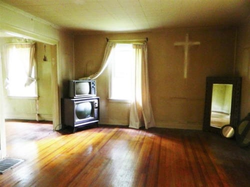 a very creepy living room with a faded cross on the wall ad stacked TVs