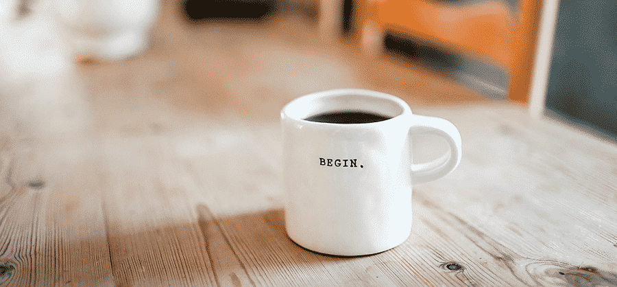 White coffee cup with the word "begin" stamped on it, sitting on wood table