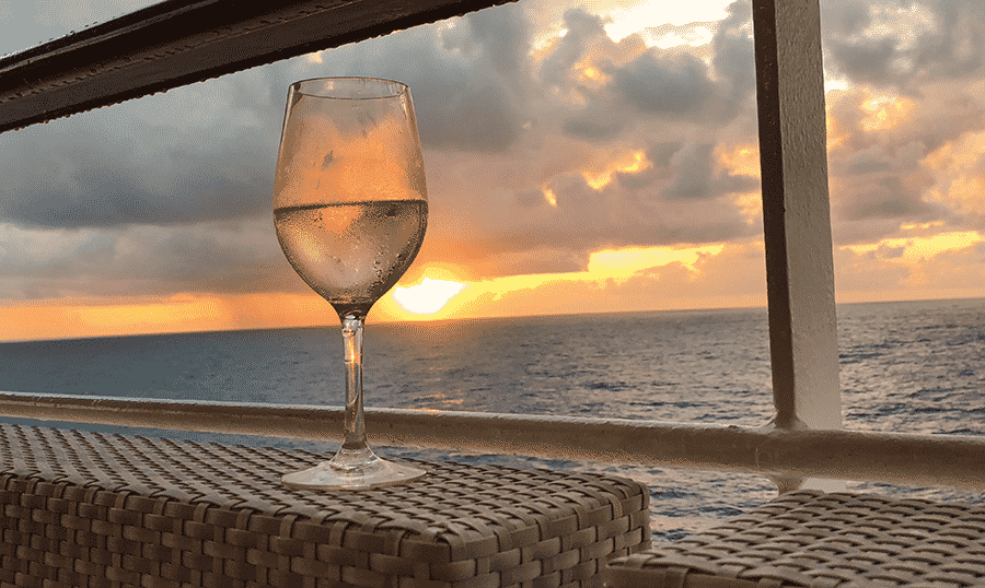 a glass of white wine overlooks a sunset over the ocean.