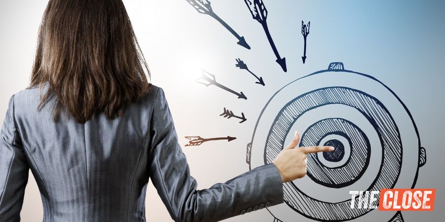 Woman facing away with her index finger pointing to the center of a bullseye drawn on a wall.