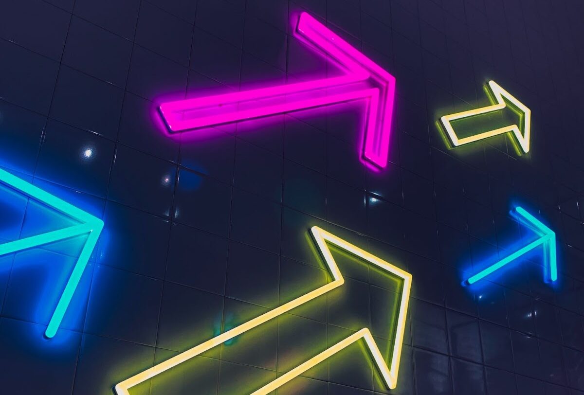 chainlink fence with dark background and multicolored neon arrows pointing up and to the right.