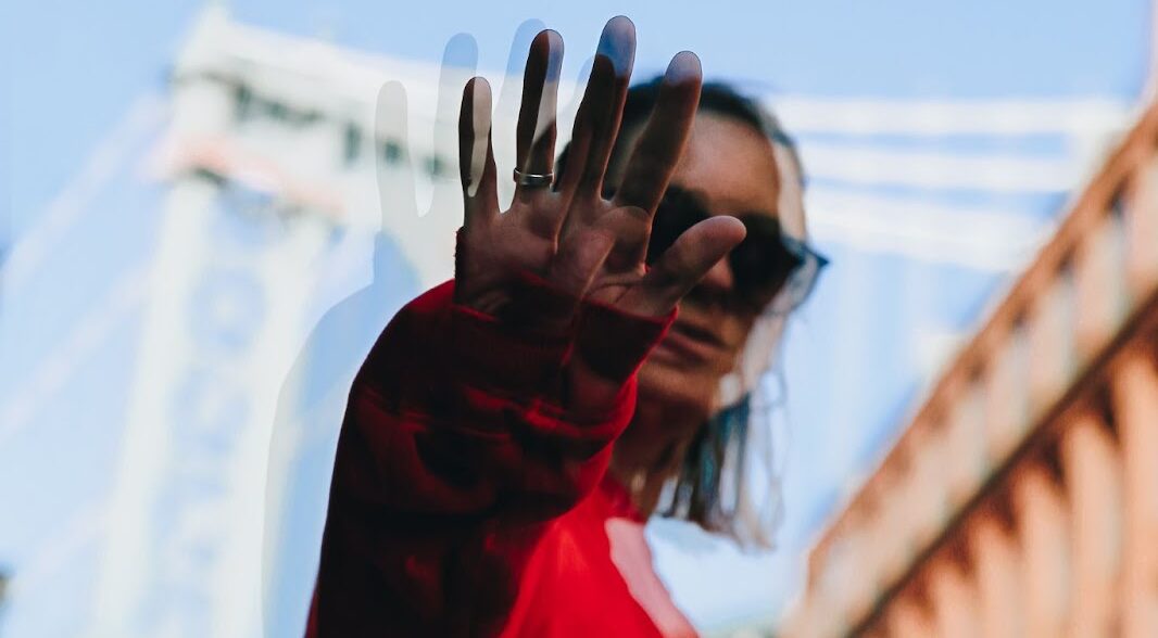 Woman standing on bridge with hand extended toward viewer