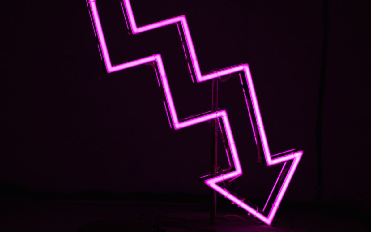 Pink neon sign depicting trend arrow moving downward on black background