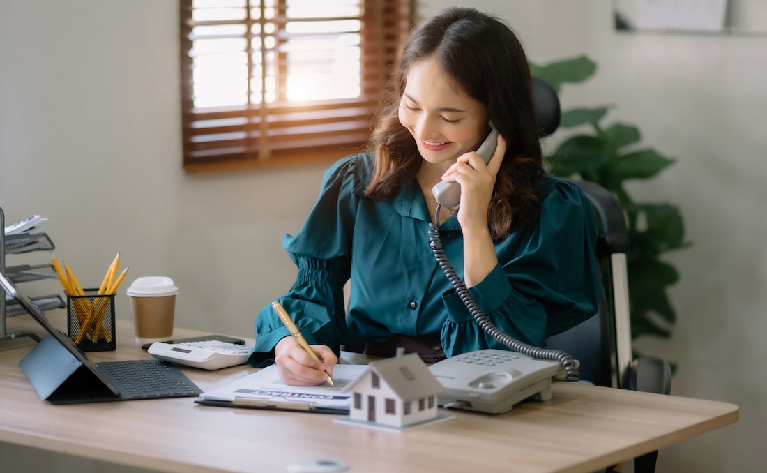 woman answering the phone with a smile on her face, jotting down information.