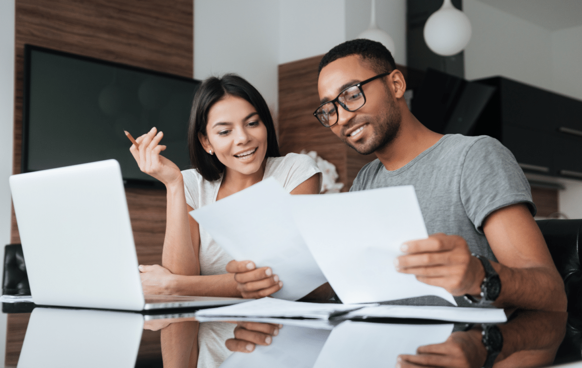 Photo of young couple sitting at a laptop, looking over some papers.