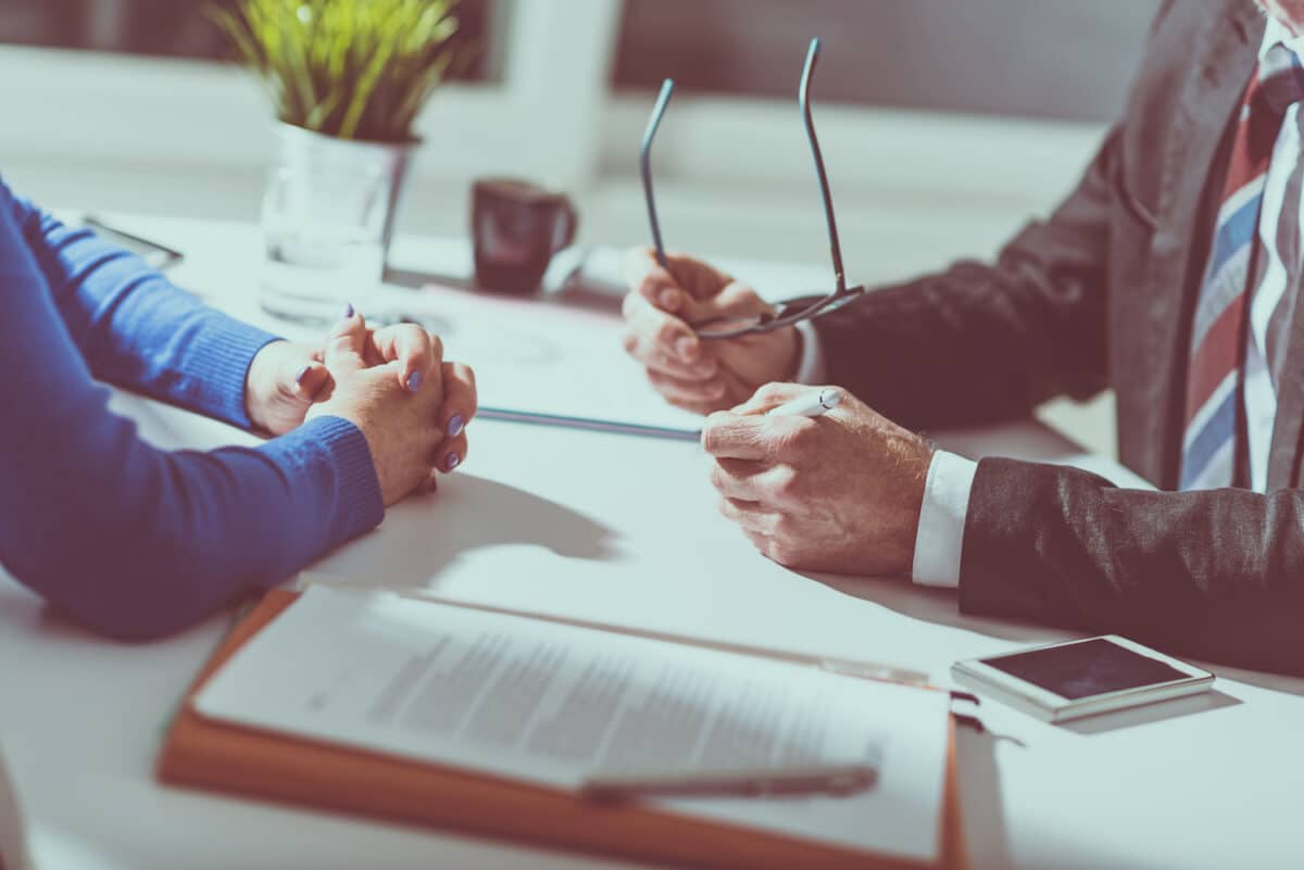 Negotiation between man and woman, table with hands, pens and a contract.