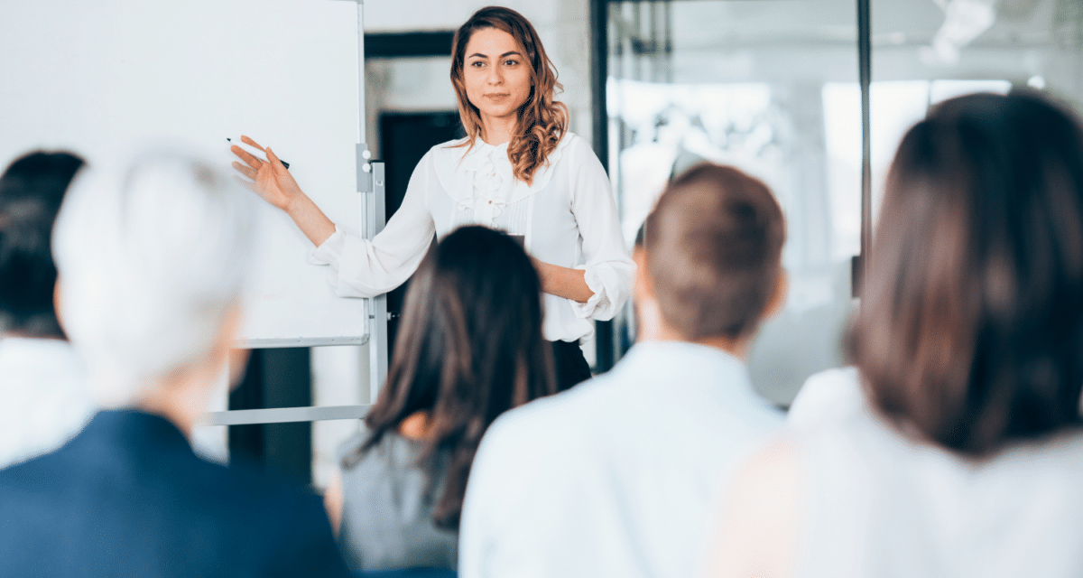 Image of a young woman talking to a group of people, educating potential buyers on the home buying process.