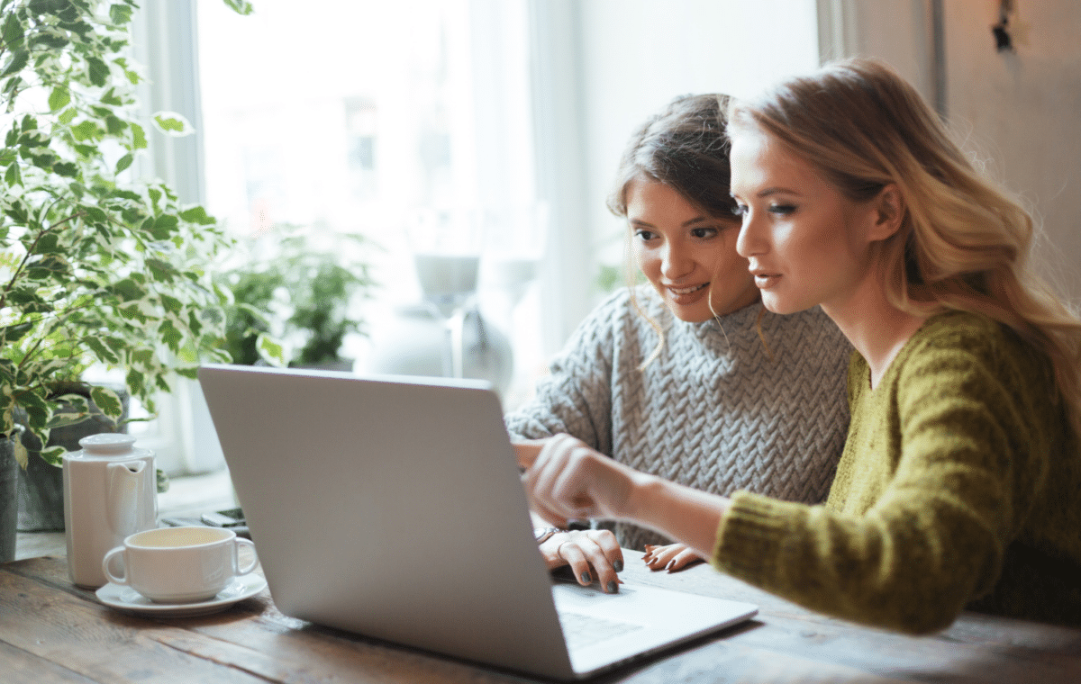 Two young women looking at a laptop together in a coffee shop.